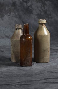Amber Whiskey Bottle, c. 1840s, glass, turned in mold; Salt-glaze Beer Bottle (with string), c.1840s, Stoneware (left); Beer Bottle (with string), c.1840s, Stoneware (right)
